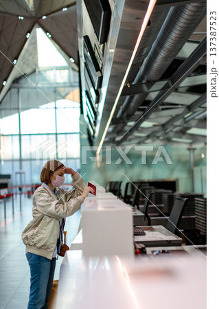 Woman in face mask over flight cancellation, stands at empty check-in counters at airport terminal.  137387523