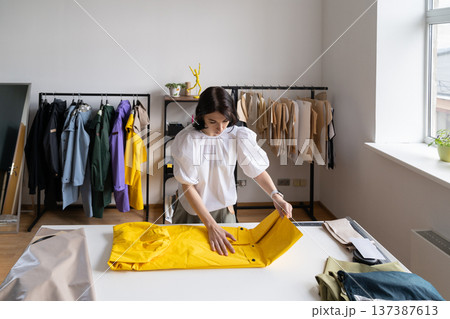 Clothes designer girl wrap raincoat of new collection after sewing in atelier. Dressmaker at work Clothes designer girl wrap raincoat of new collection after sewing in atelier. Dressmaker at work 137387613