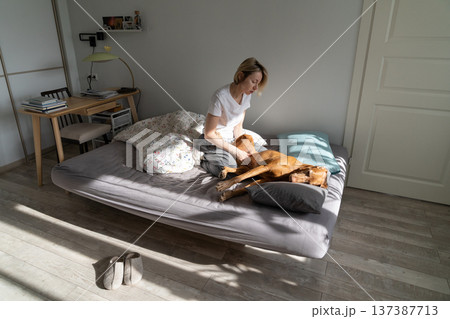 Melancholy pensive woman middle age sits in bedroom on bed and petting dog to get rid of depression Melancholy pensive woman middle age sits in bedroom on bed and petting dog to get rid of depression 137387713