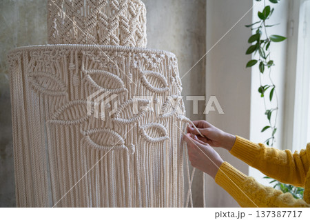 Clos up of woman working on half-finished macrame piece, weaves lamp shade for chandelier. hobby. 137387717