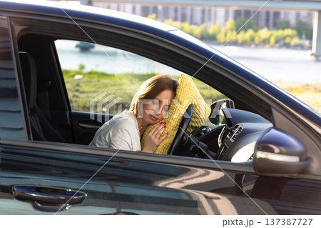 Tired woman driver asleep on pillow on steering wheel, resting after long hours driving car. Fatigue Tired woman driver asleep on pillow on steering wheel, resting after long hours driving car. Fatigue 137387727