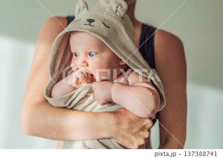 Mother holding her baby wrapped in a soft towel after bath at home, sharing a warm caring moment. Authentic parenthood scene showing love, safety and comfort. Baby hygiene, wellbeing and family 137388741