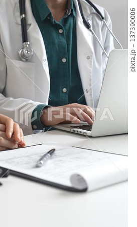 Doctor man wearing lab coat over a green shirt, is typing on a laptop and listening to a woman patient during medical consultation in clinic. Medicine and health care Doctor man wearing lab coat over a green shirt, is typing on a laptop and listening to a woman patient during medical consultation in clinic. Medicine and health care 137390006