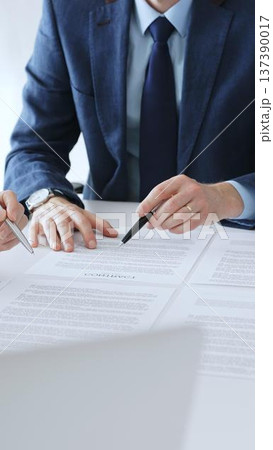 Businesspeople hands with pens reviewing documents and engaging in a discussion across a table, representing contract signing, legal consultation, negotiation, and important agreement collaboration 137390017