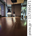 Long wooden table with reflections under three hanging black pendant lights in a dimly lit room. The ceiling has exposed ducts and a light-colored acoustic panel 137390471