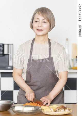キッチンで野菜を切り料理の下ごしらえをするシニア女性 137393357