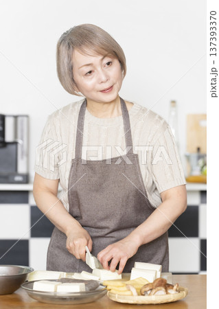 キッチンで野菜を切り料理の下ごしらえをするシニア女性 137393370
