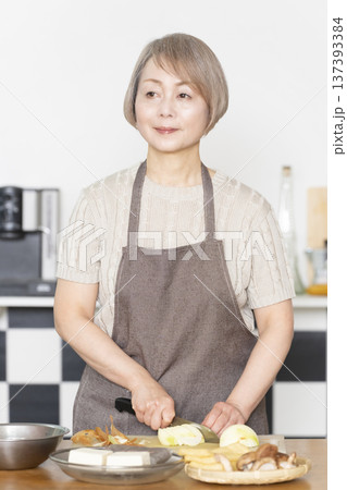 キッチンで野菜を切り料理の下ごしらえをするシニア女性 137393384