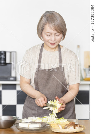 キッチンで野菜を切り料理の下ごしらえをするシニア女性 137393394