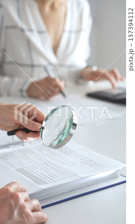 Team of accountants are working together, using a magnifying glass and a calculator, to audit financial reports in office. Audit and taxes concept 137394112