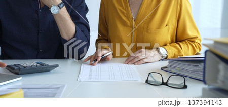 Professional accountants collaborating in a well lit office, analyzing financial data and discussing statements with a calculator and pen. Audit and taxes theme in business 137394143