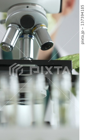 Close up of a scientist in green gloves and a mask using a microscope for research and analysis in a laboratory setting. Medicine, healthcare and science concept 137394185