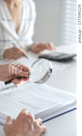 Team of accountants are working together, using a magnifying glass and a calculator, to audit financial reports in office. Audit and taxes concept 137394229