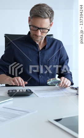 Businessman working in office set is using calculator and magnifying glass analyzing financial documents, performing accounting and financial analysis. Audit and taxes concept 137394244
