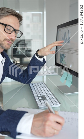 Professional businessman in a blue jacket working on desktop computer in modern office, focusing on his work and business tasks. Business people concept 137394262