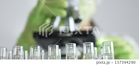 Close up of test tubes with a scientist analyzing plant samples in test tubes with a microscope in a laboratory at the background. Medicine, healthcare and science concept Close up of test tubes with a scientist analyzing plant samples in test tubes with a microscope in a laboratory at the background. Medicine, healthcare and science concept 137394290