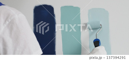 Painter wearing protective gloves rolling blue paint on white wall, creating gradient color effect for home interior renovation project Painter wearing protective gloves rolling blue paint on white wall, creating gradient color effect for home interior renovation project 137394291