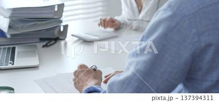 Professional team collaborating, reviewing financial reports, using calculator, analyzing data while working at sleek corporate workspace. Audit and taxes in business Professional team collaborating, reviewing financial reports, using calculator, analyzing data while working at sleek corporate workspace. Audit and taxes in business 137394311