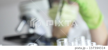 Close up of test tubes with a scientist analyzing plant samples in test tubes with a microscope in a laboratory at the background. Medicine, healthcare and science concept Close up of test tubes with a scientist analyzing plant samples in test tubes with a microscope in a laboratory at the background. Medicine, healthcare and science concept 137394314