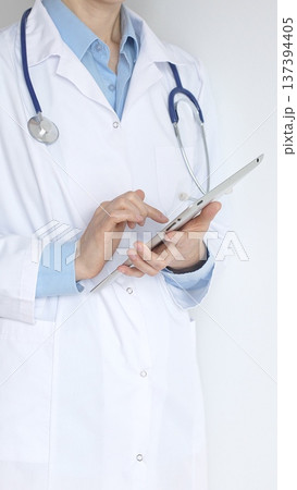 Close up of female doctor, wearing white coat over a blue blouse and a stethoscope, is using a digital tablet, suggesting innovative healthcare practices in medicine. Health care and medicine concept 137394405