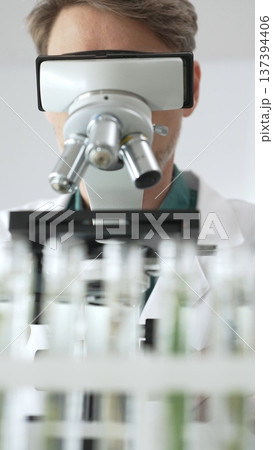 Man scientific researcher in protective gear analyzing specimens through a microscope in a sterile laboratory environment. Medicine, health care and science concept Man scientific researcher in protective gear analyzing specimens through a microscope in a sterile laboratory environment. Medicine, health care and science concept 137394406
