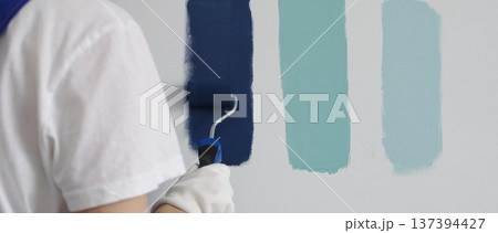 Painter wearing protective gloves rolling blue paint on white wall, creating gradient color effect for home interior renovation project Painter wearing protective gloves rolling blue paint on white wall, creating gradient color effect for home interior renovation project 137394427