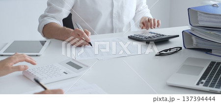 Professional accountants collaborating in a well lit office, analyzing financial data and preparing reports with calculators and pens. Audit and taxes Professional accountants collaborating in a well lit office, analyzing financial data and preparing reports with calculators and pens. Audit and taxes 137394444