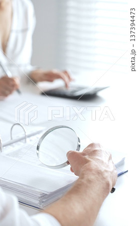 Close up of accountant hand using a magnifying glass and a calculators, to audit financial reports in brightly lit office. Audit and taxes concept Close up of accountant hand using a magnifying glass and a calculators, to audit financial reports in brightly lit office. Audit and taxes concept 137394473