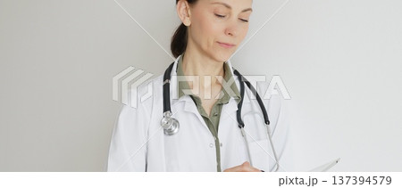 Confident doctor woman female medical professional wearing lab coat over green blouse and stethoscope is using digital tablet, representing modern healthcare and medical technology. Medicine concept 137394579
