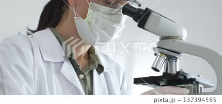 Female scientist examining microscope slide, wearing protective gear while conducting medical research in sterile laboratory environment. Medicine, healthcare and science concept 137394585