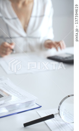 Magnifying glass on financial documents, with an accountant using a calculator and taking notes, emphasizing accounting, finance, and tax preparation, close up vertical view. Audit and taxes Magnifying glass on financial documents, with an accountant using a calculator and taking notes, emphasizing accounting, finance, and tax preparation, close up vertical view. Audit and taxes 137394619