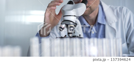 Male scientist wearing lab coat and protective glasses using microscope doing research in modern laboratory setup, portrait view. Low key lighting photo. Science and Medicine concept Male scientist wearing lab coat and protective glasses using microscope doing research in modern laboratory setup, portrait view. Low key lighting photo. Science and Medicine concept 137394624
