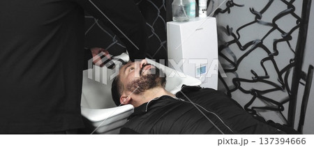 Professional hairdresser rinsing client's hair in sleek salon, urban graffiti backdrop highlighting contemporary styling environment during cleansing process 137394666