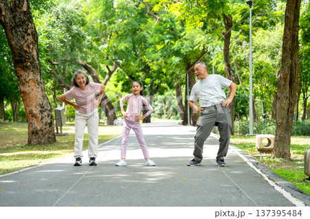 Front view of Asian senior man and woman also the girl action of stretching the waist and they look happy in public park together. Front view of Asian senior man and woman also the girl action of stretching the waist and they look happy in public park together. 137395484