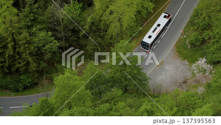 Bus travels along winding road surrounded by green trees in a rural area during daytime Bus travels along winding road surrounded by green trees in a rural area during daytime 137395563