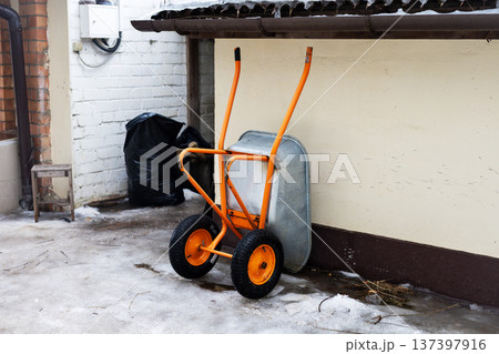 Weathered hand cart in snowy alleyway. Old industrial trolley rests against chipped brick wall 137397916