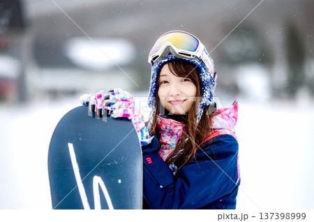 スキー場のゲレンデでウィンタースポーツのスノーボードを楽しむ若い女性 137398999