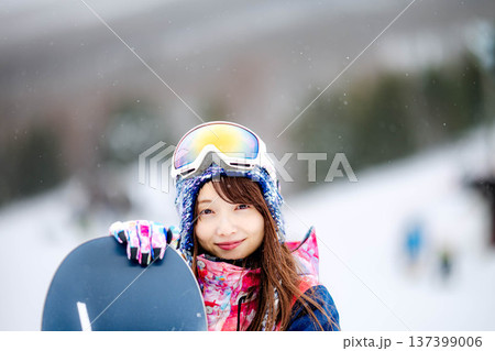 スキー場のゲレンデでウィンタースポーツのスノーボードを楽しむ若い女性 137399006