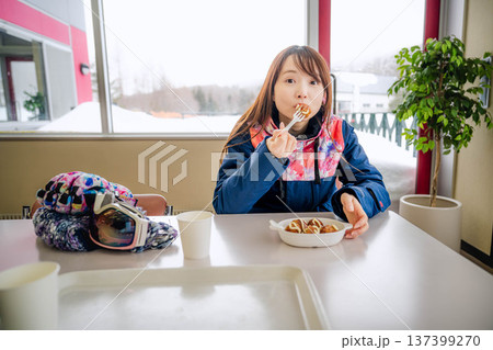 スキーウェアを着て休憩しながら食事をとる若い女性 137399270