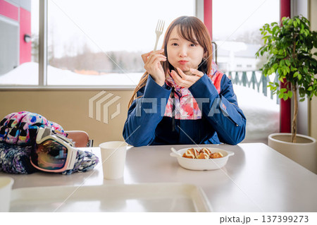 スキーウェアを着て休憩しながら食事をとる若い女性 137399273