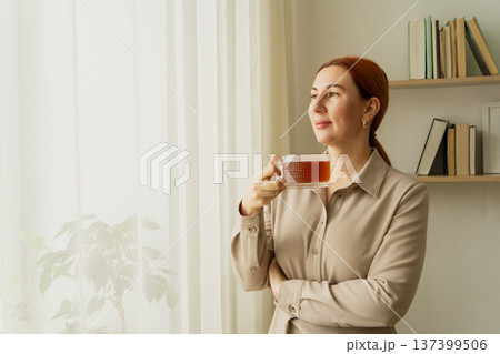 Woman drinking tea looking out window thoughtfully. Women's mental health, balance Woman drinking tea looking out window thoughtfully. Women's mental health, balance 137399506