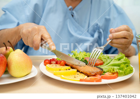 Asian elderly woman patient eating salmon stake and vegetable salad for healthy food in hospital. Asian elderly woman patient eating salmon stake and vegetable salad for healthy food in hospital. 137401042