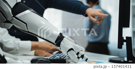 Futuristic Robot Arm Interacting with Computer Display in Modern Office Environment Highlighting Collaboration Between Technology and Human Workforce. Noogenesis 137401431
