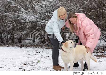 Two women interacting with dog outdoors in winter 137403107