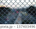金網フェンス越しに見える車のライトの玉ボケと夕暮れの空 137403496