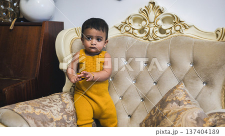 Cute baby boy in yellow romper standing on a traditional sofa at home 137404189