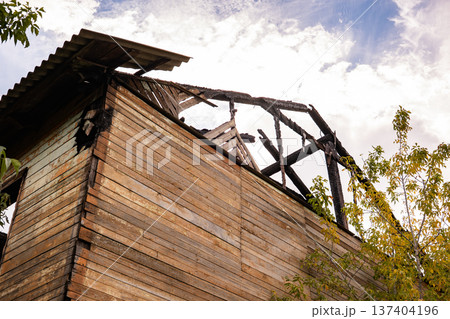 Burnt wooden house with destroyed roof showing fire damage and abandonment Burnt wooden house with destroyed roof showing fire damage and abandonment 137404196