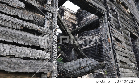Charred remains of a burned down wooden house with textured charcoal logs 137404227