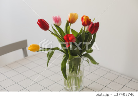 Fresh spring colorful bouquet of tulips in vase standing on white table in light classic design living room background. Festive flowers for gift. Mockup for greeting card Fresh spring colorful bouquet of tulips in vase standing on white table in light classic design living room background. Festive flowers for gift. Mockup for greeting card 137405746
