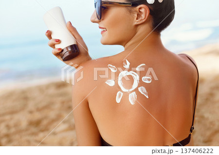 Young woman with sun cream on shoulder holding sunscren bottle on the beach. Female in hat applying moisturizing lotion on skin.SkinCare.Suntan Young woman with sun cream on shoulder holding sunscren bottle on the beach. Female in hat applying moisturizing lotion on skin.SkinCare.Suntan 137406222